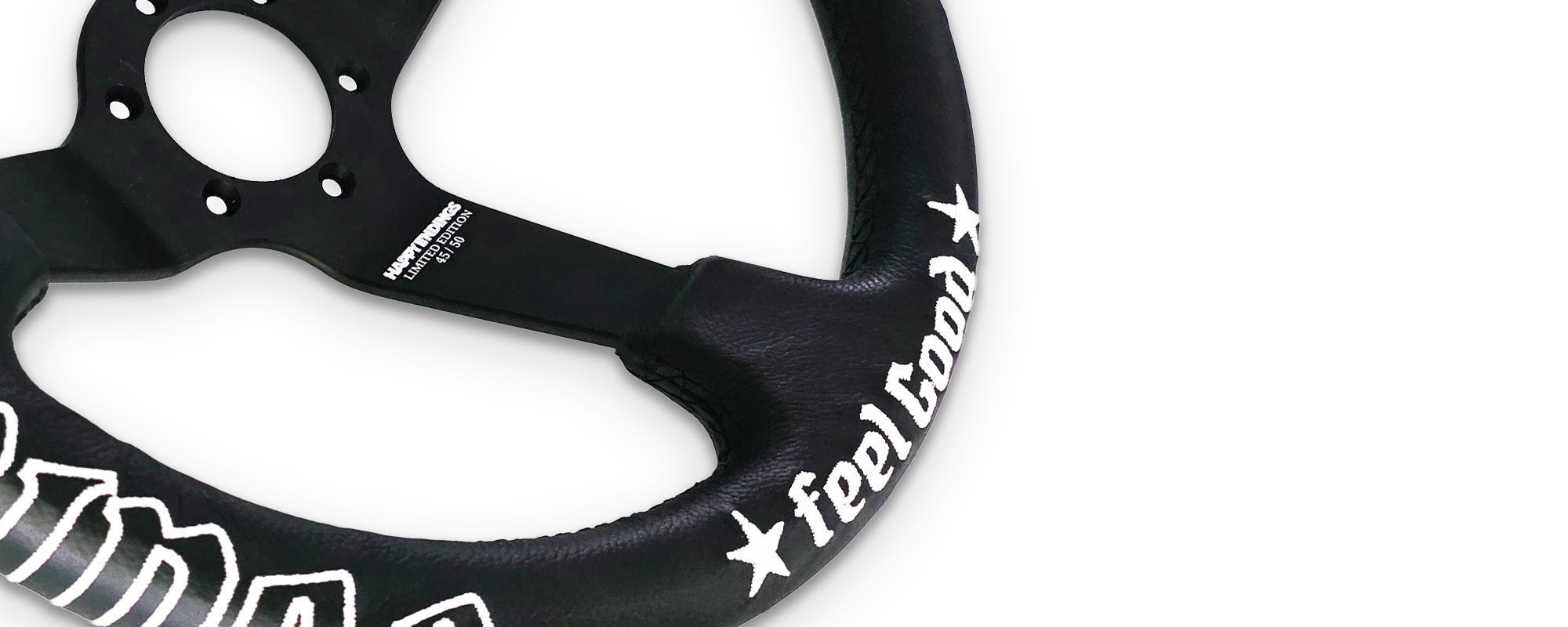 Black deep-dish steering wheel with white embroidered stitching, red center stripe, matte black 3-spoke design, and JDM-inspired “feel good” script embroidery.