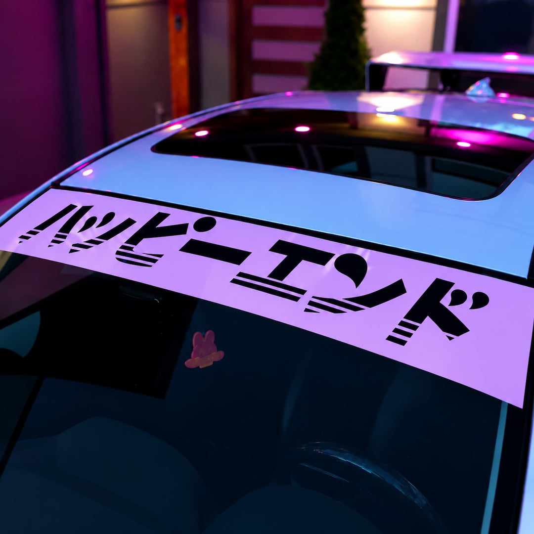 Car windshield banner with the Japanese text Happy End in black stylized font.
