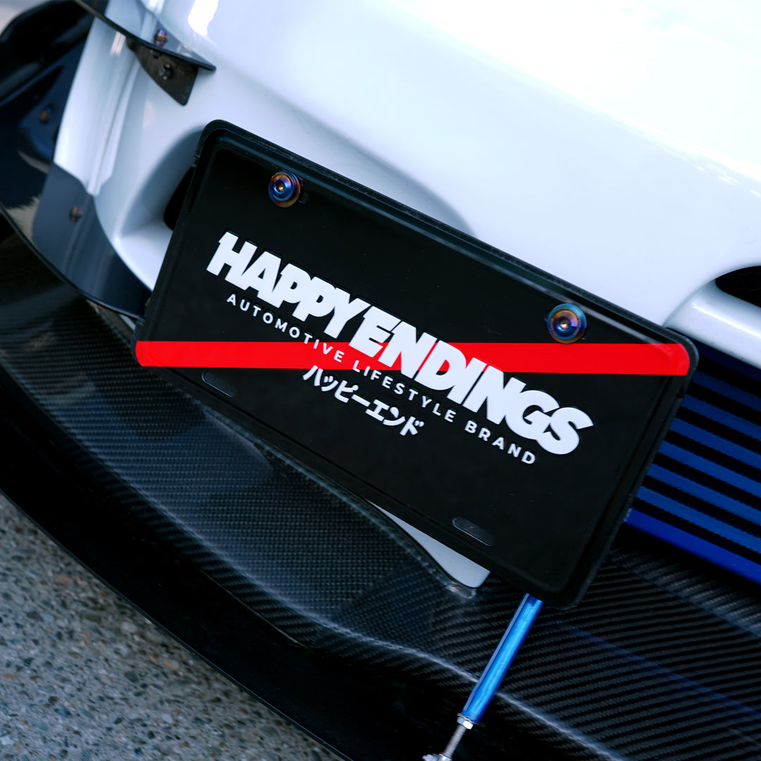 Black license plate with HAPPY ENDINGS and Japanese text on a white sports car.