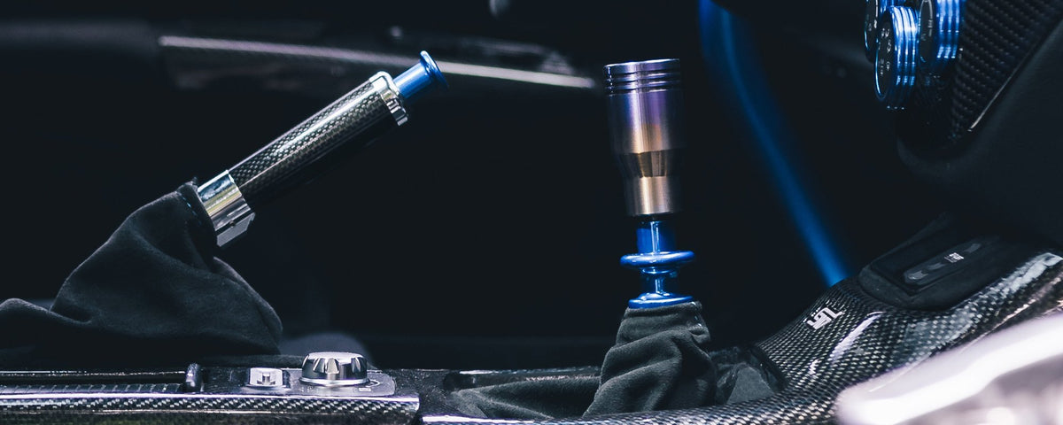 Close-up of a car’s gear shift and handbrake, both with blue accents, in a carbon fiber-trimmed interior.