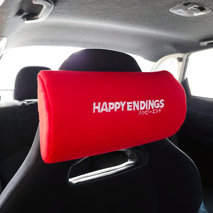 Red neck pillow with 'HAPPY ENDINGS' text in a car interior