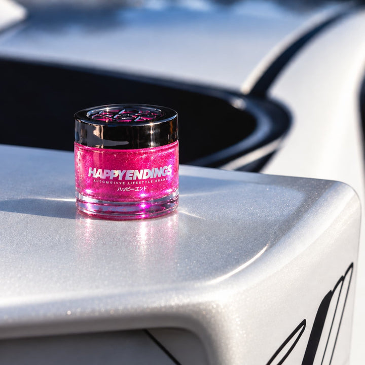 A small jar labeled HAPPY ENDINGS with pink gel sits on a shiny white surface.