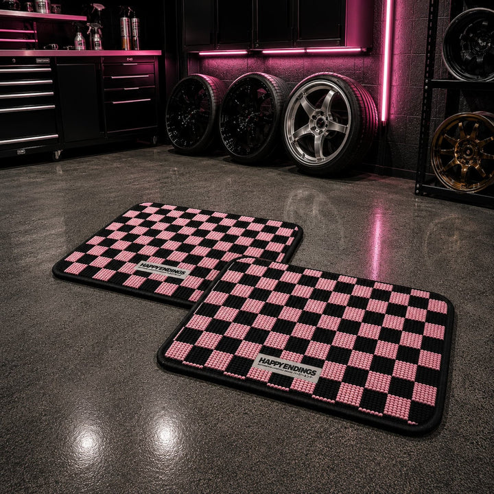 Two pink and black checkered mats on a shiny garage floor, with rims and neon lights in the background.