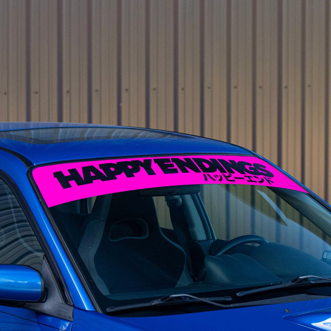 Bright pink HAPPY ENDINGS banner with Japanese text on a blue car windshield.