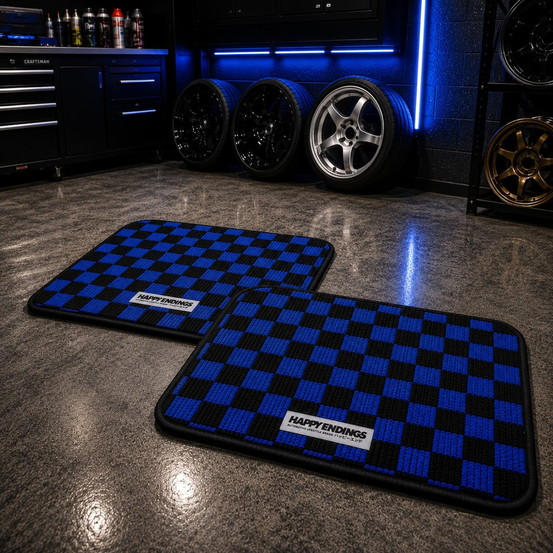 Two blue-and-black checkerboard floor mats on a garage floor, with wheels and...