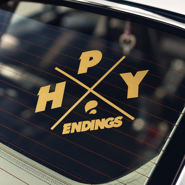 A gold decal on a car window reading HPY ENDINGS arranged in a cross pattern.
