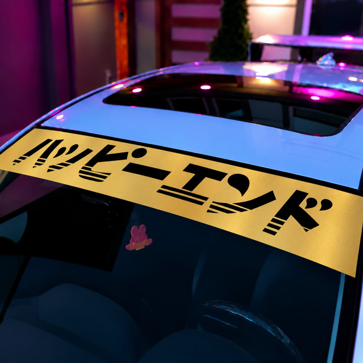 A yellow car windshield banner with the Japanese text Happy End in black.