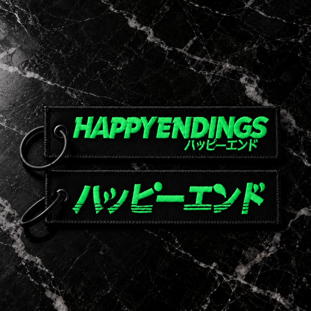 Two black embroidered keychains featuring the text HAPPY ENDINGS and Japanese...