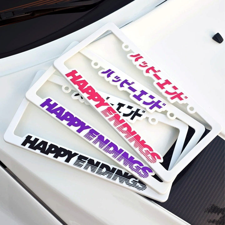 Three white license plate frames with HAPPY ENDINGS in English and Japanese text on a car hood.