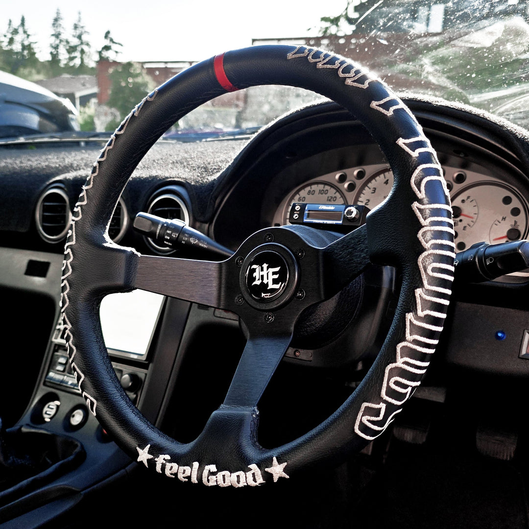 Black deep-dish steering wheel with white embroidered stitching, matte black 3-spoke design.
