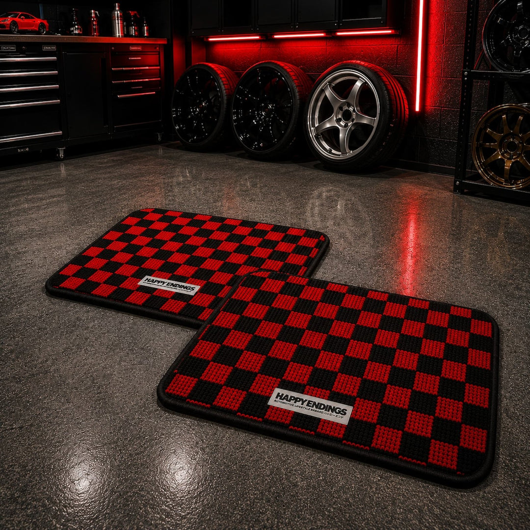 Two red and black checkered floor mats in a garage with car wheels and red li...