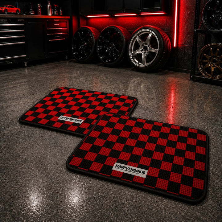 Two red and black checkered floor mats in a garage with car wheels and red lighting in the background.
