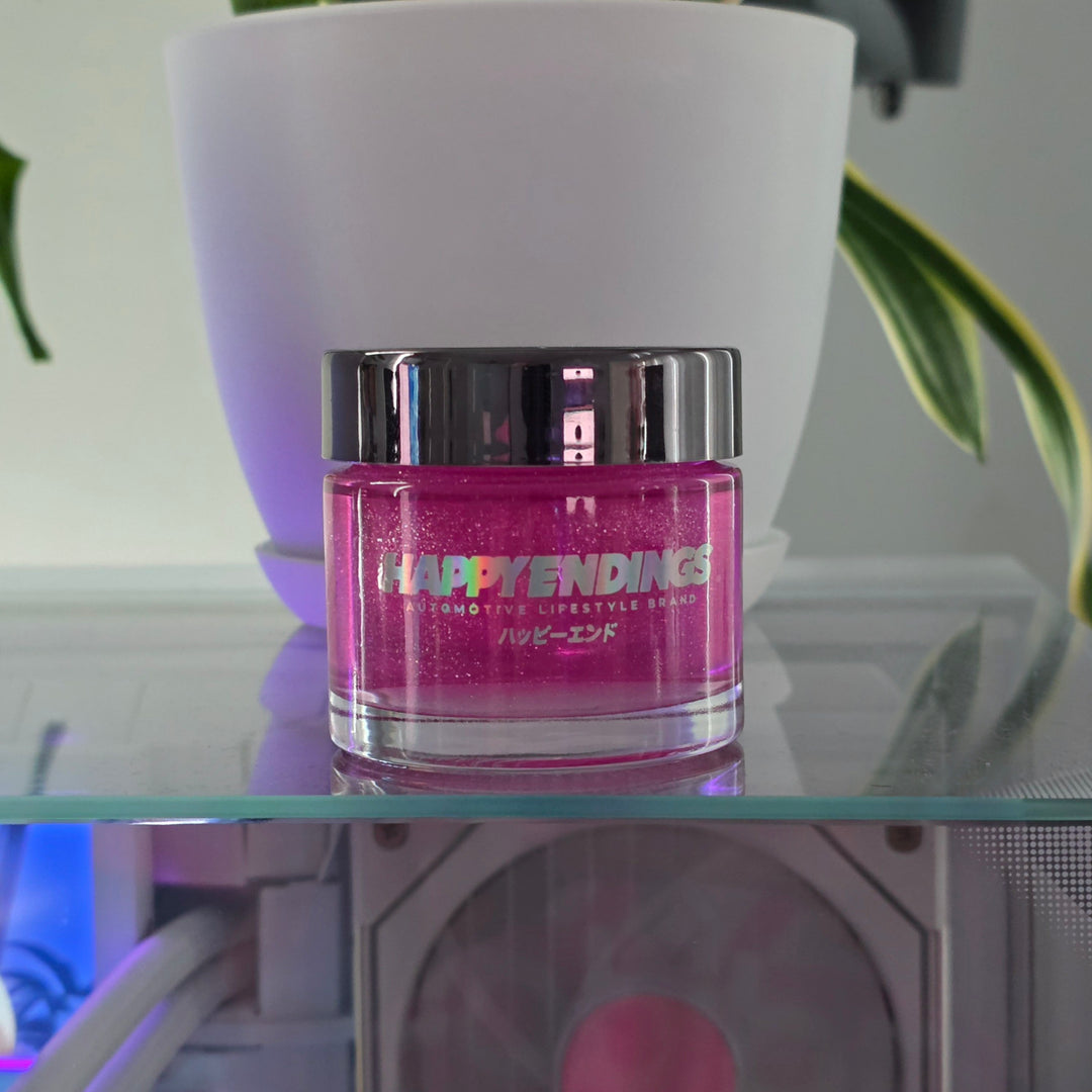 Small pink jar labeled Happy Endings in front of a white plant pot on a glass surface.