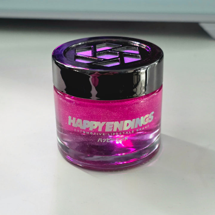 Small pink jar labeled HAPPY ENDINGS with a shiny black lid on a white surface.