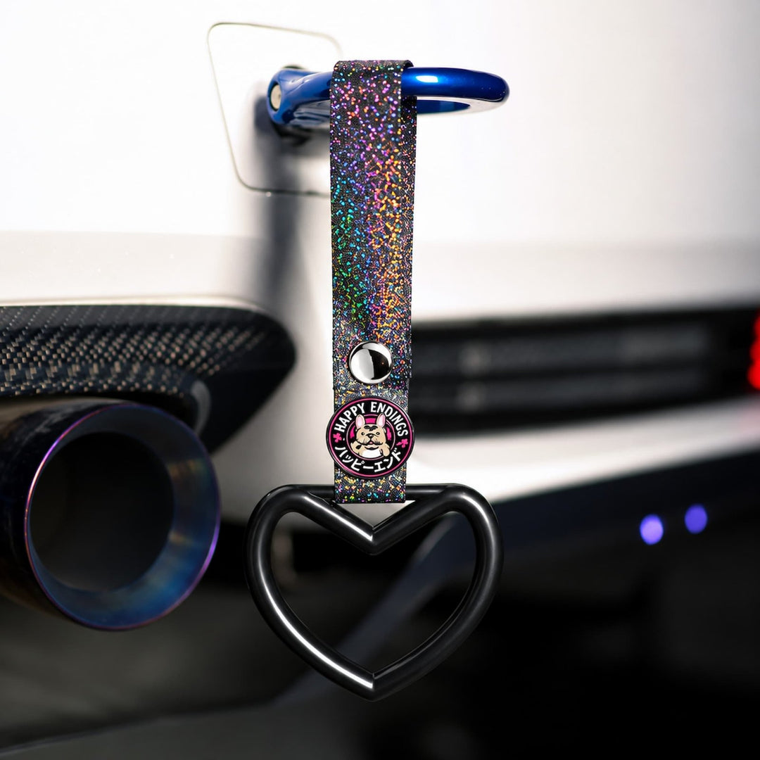 A glittery keychain with a heart shape and Happy Endings charm hangs from a car part.