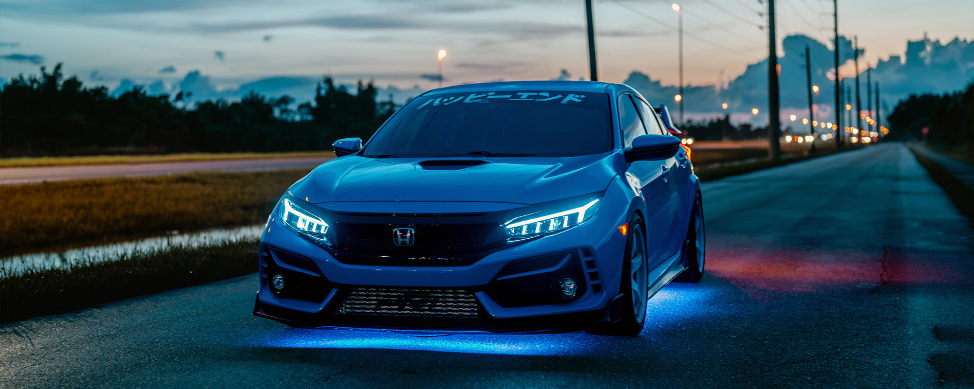 Blue Honda Civic on a road at dusk with city lights in the background