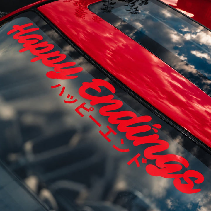 Red car windshield with a decal that says Happy Endings in English and Japanese.
