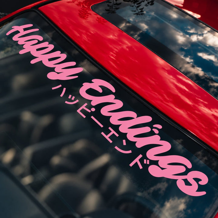 Pink Happy Endings text decal in English and Japanese on a red car windshield.
