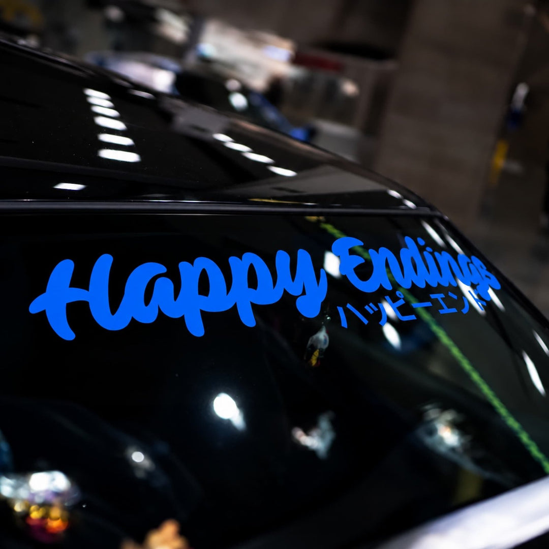 Blue Happy Endings decal written in English and Japanese on a cars rear windshield.