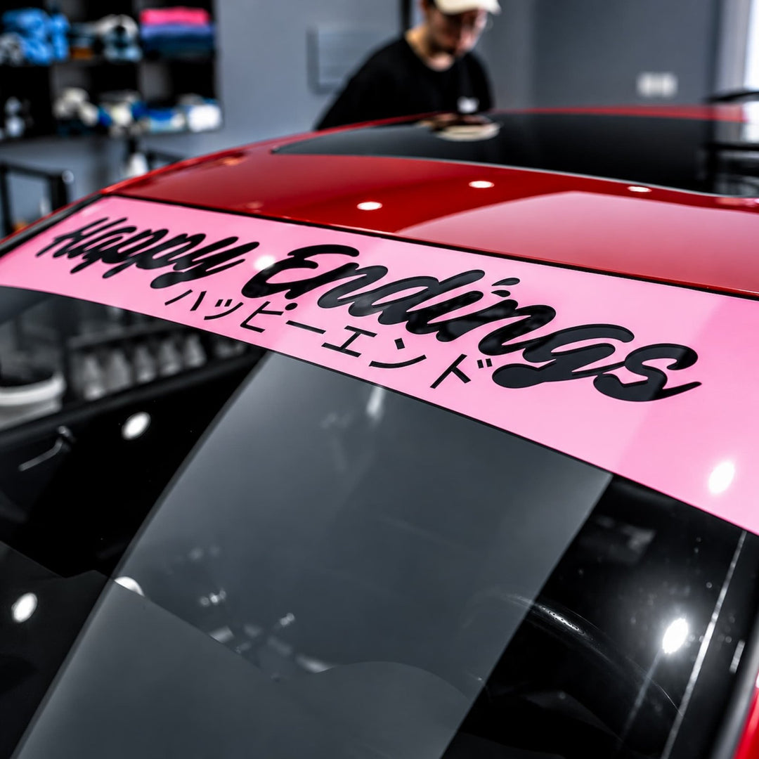 A pink windshield banner reads Happy Endings and Japanese text on a red and black car.