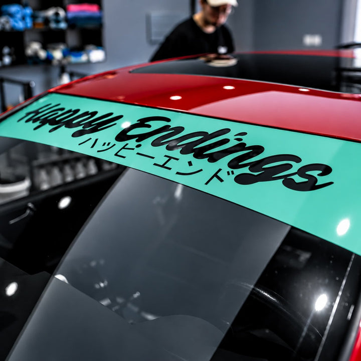 Close-up of a car windshield banner reading Happy Endings and Japanese text.