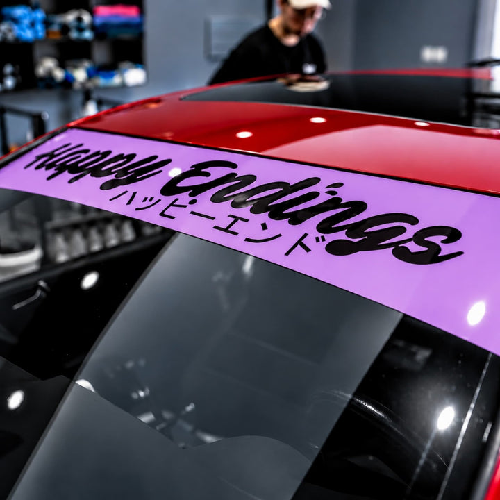 Red car windshield with a purple banner reading Happy Endings in English and Japanese.