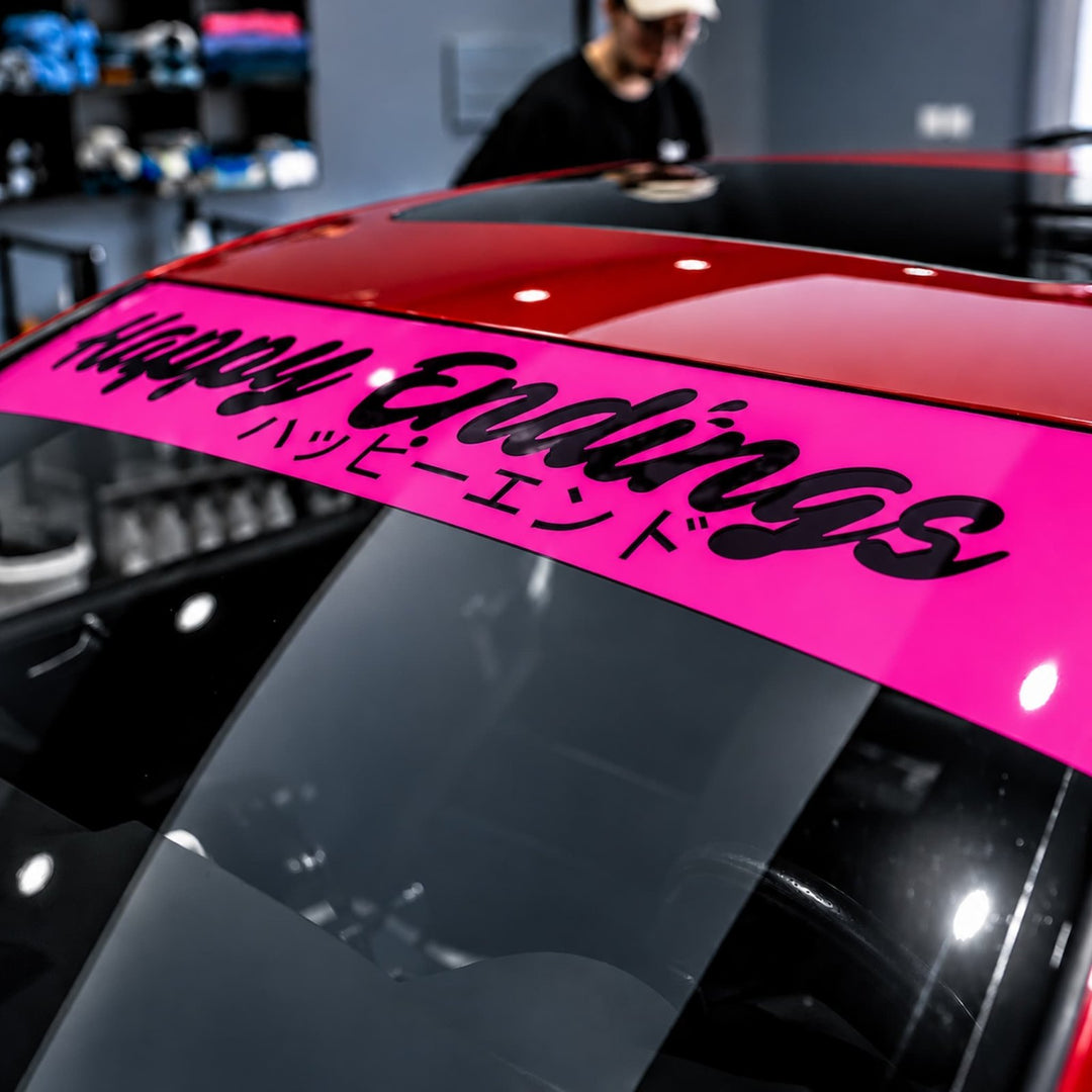 Pink windshield banner on car reads Happy Endings with Japanese text below.