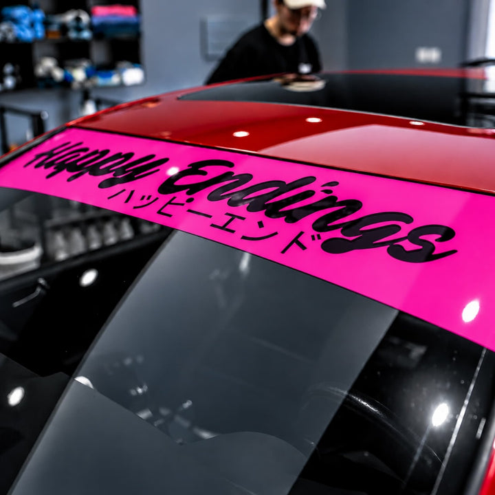 Pink windshield banner on car reads Happy Endings with Japanese text below.