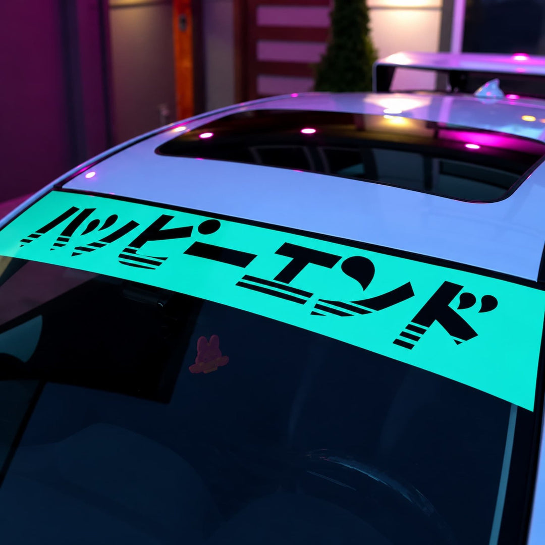 A car windshield decal in Japanese Katakana, glowing under colorful lights at night.