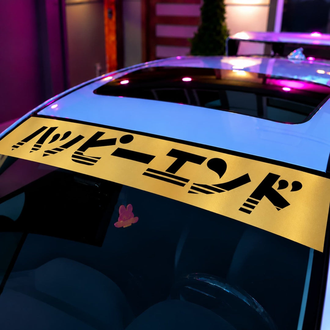 A yellow car windshield banner with the Japanese text Happy End in black.