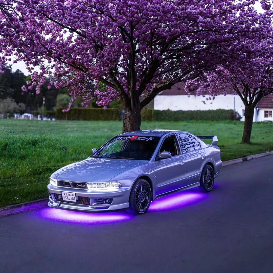 Silver car with purple underglow parked under blooming cherry blossom trees a...