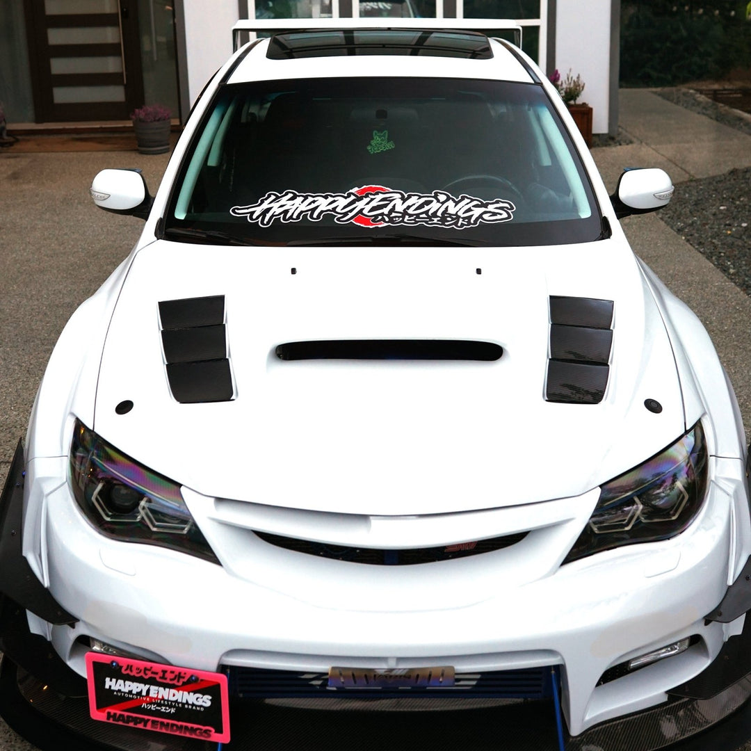 Front view of a white customized Subaru hatchback with Happy Endings decals.