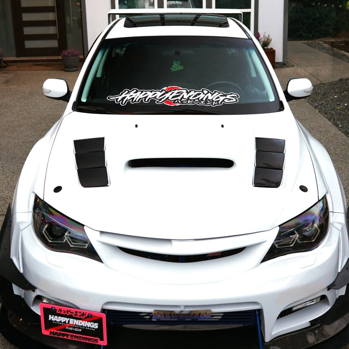 Front view of a white customized Subaru hatchback with Happy Endings decals.