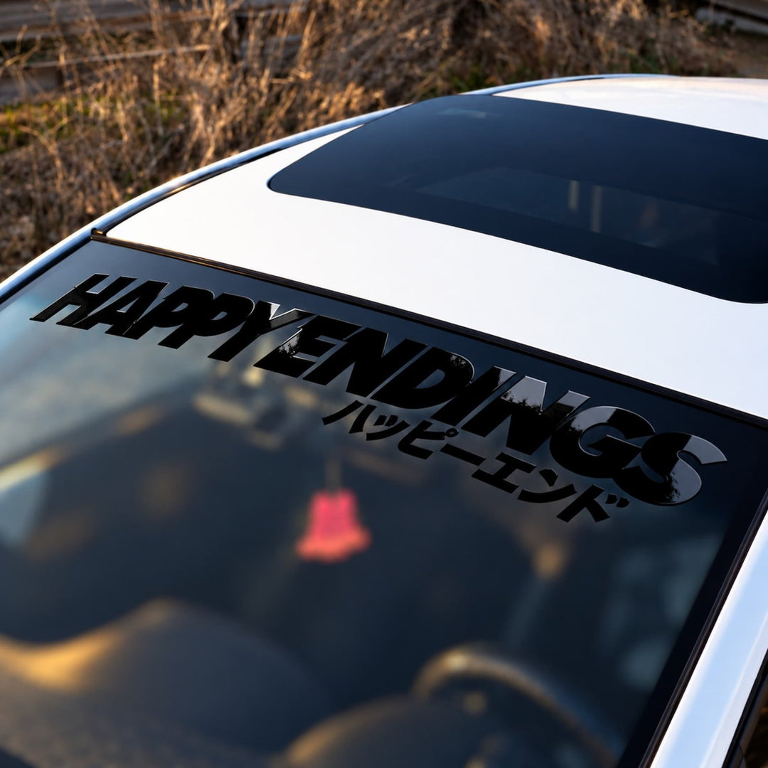 White car windshield with a decal reading HAPPY ENDINGS in English and Japanese text.
