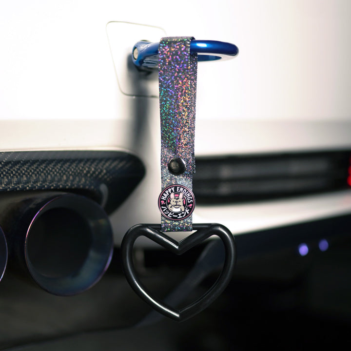 Glittery keychain with a heart-shaped ring and a Happy Everyday pin, hanging on a car dashboard air vent.